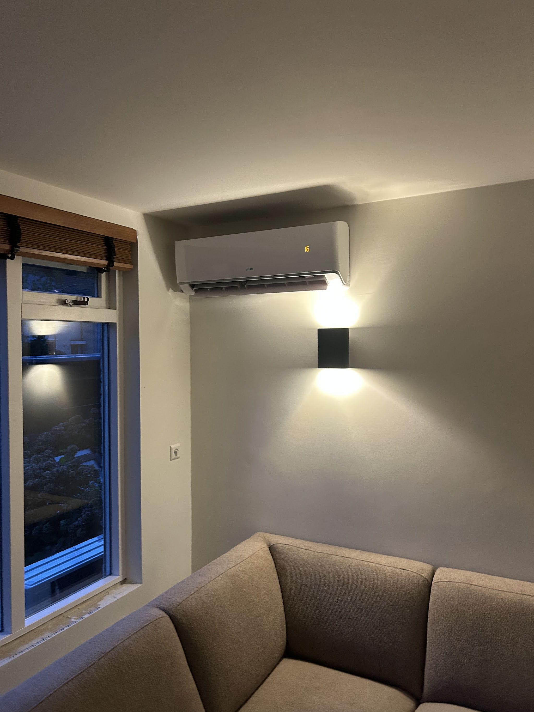 Witte airco-binnenunit boven het raam in een woonkamer, 's avonds